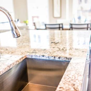 New modern faucet and kitchen room sink closeup with island and granite countertops in model house, home, apartment